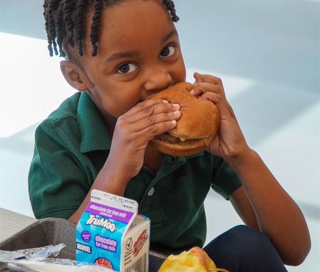 An African American child taking a big bite of a burger.
