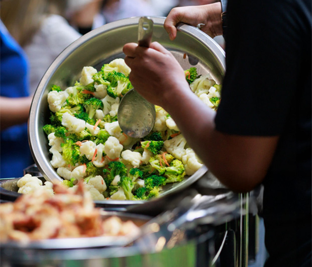 A server souping out a tossed salad in a large bowl.