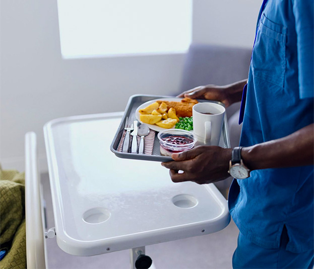 A healthcare worker taking a metal tray full of food.