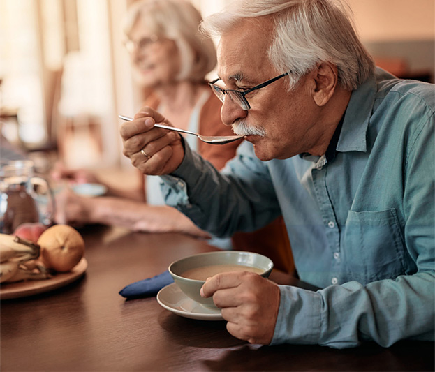 An older man taking a taste of soup.