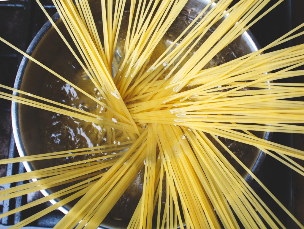 A top down photo of a raw noddles in a boiling pot.