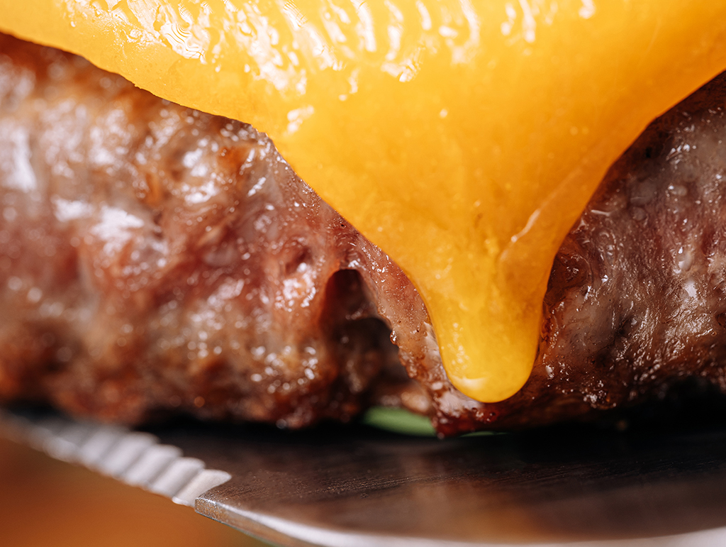 An extreme close up of a burger with yellow cheese melting down the side.
