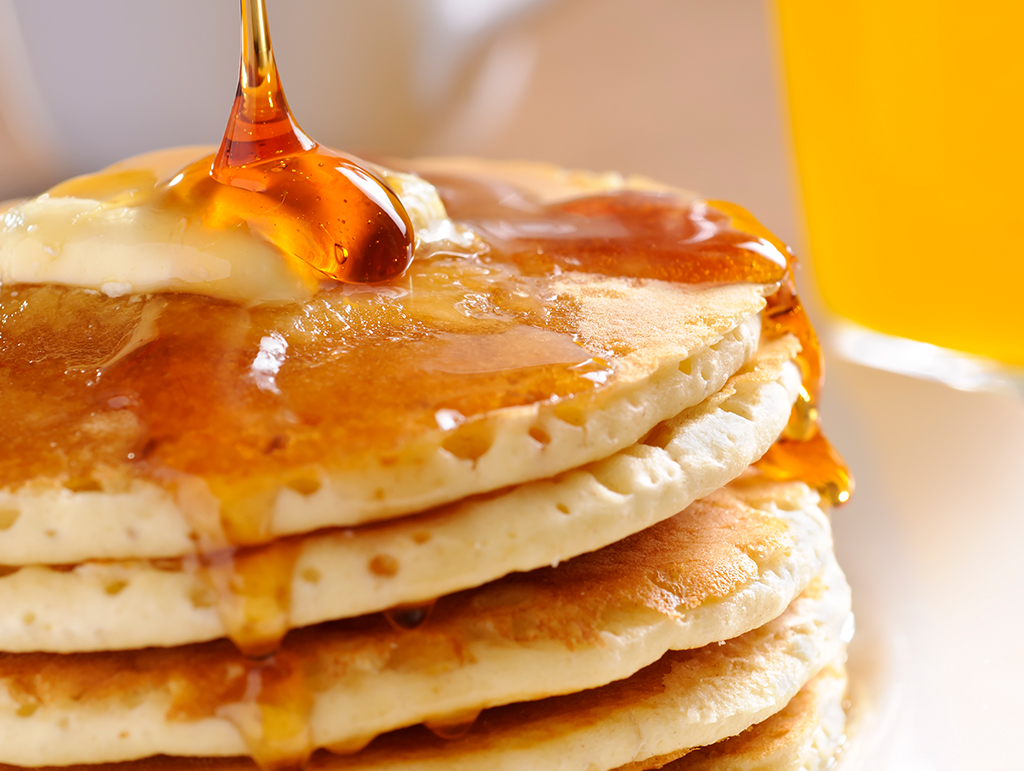 A big stack of pancakes with syrup pouring down.
