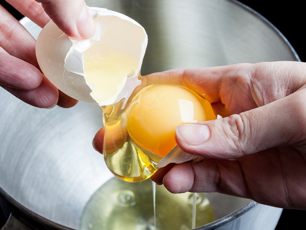 A close up of a cracked egg being handled to strained the egg whites.