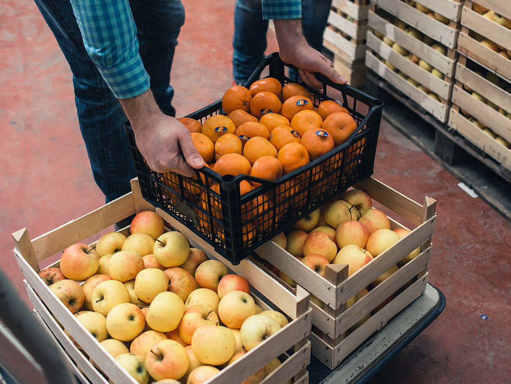 A farmer handling a wooden crate of oranges.