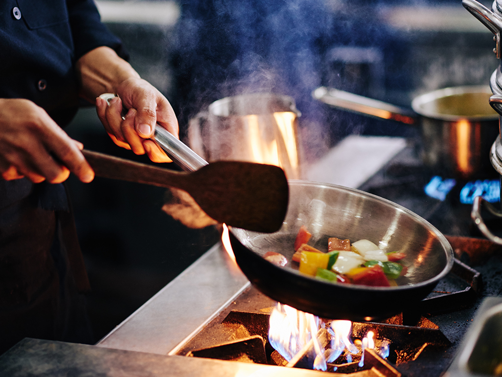 A chef flambé a pan of vegetables.