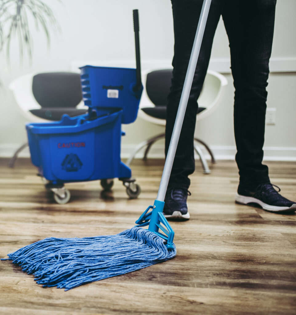 A worker using a blue mop to clean the floor.