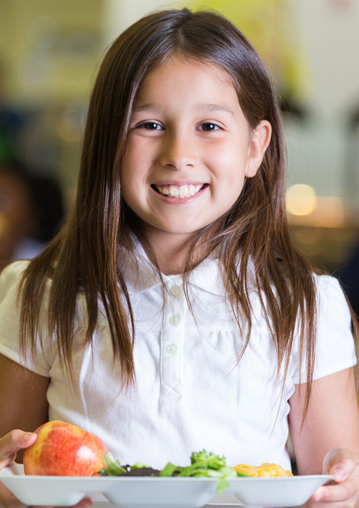 A young girl hold a tray of food in a cafeteria.